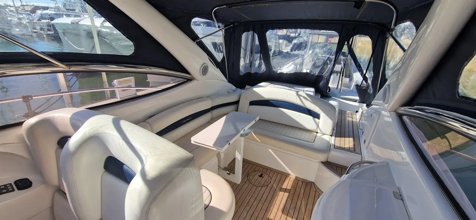 Interior of a luxury boat featuring leather seating, a small table, and panoramic windows overlooking a marina.